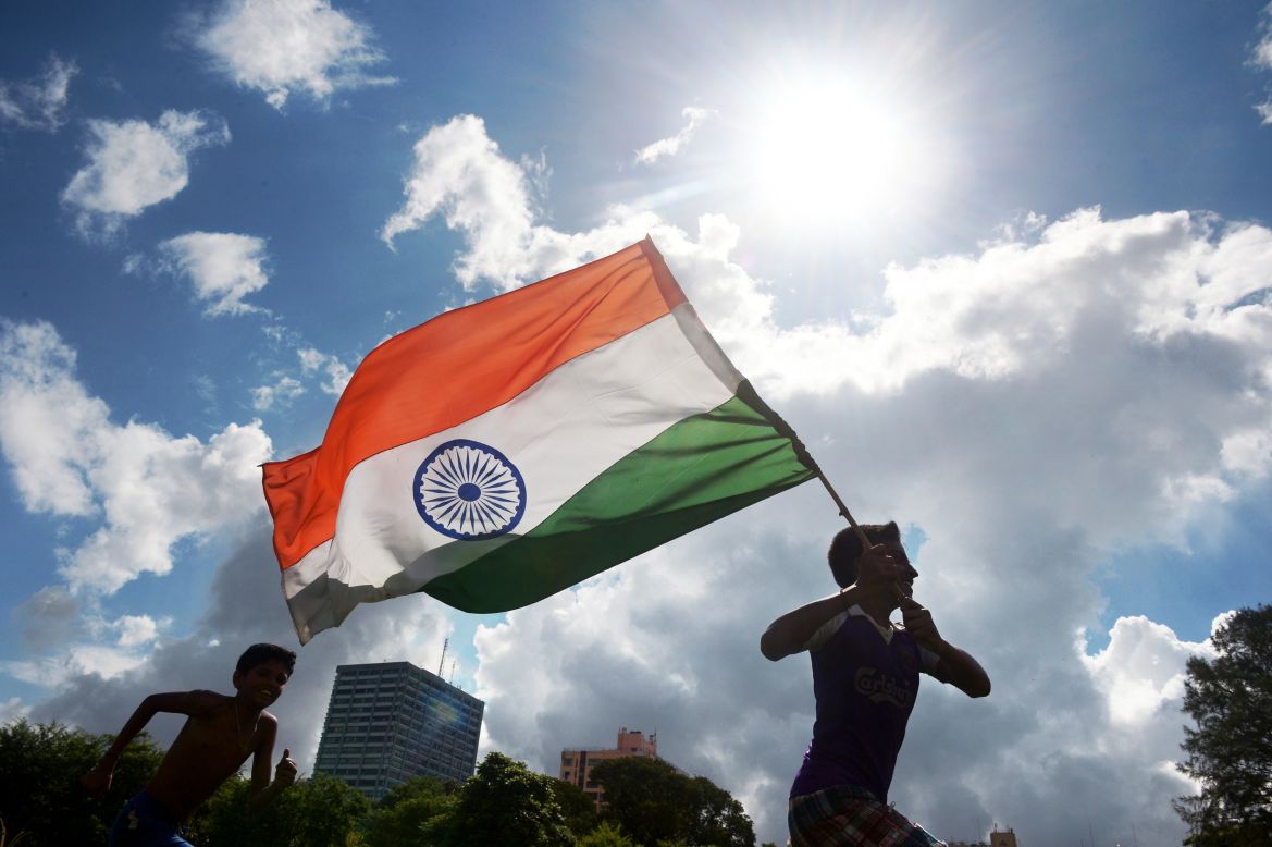 Indian youths run in a field with their national flag.