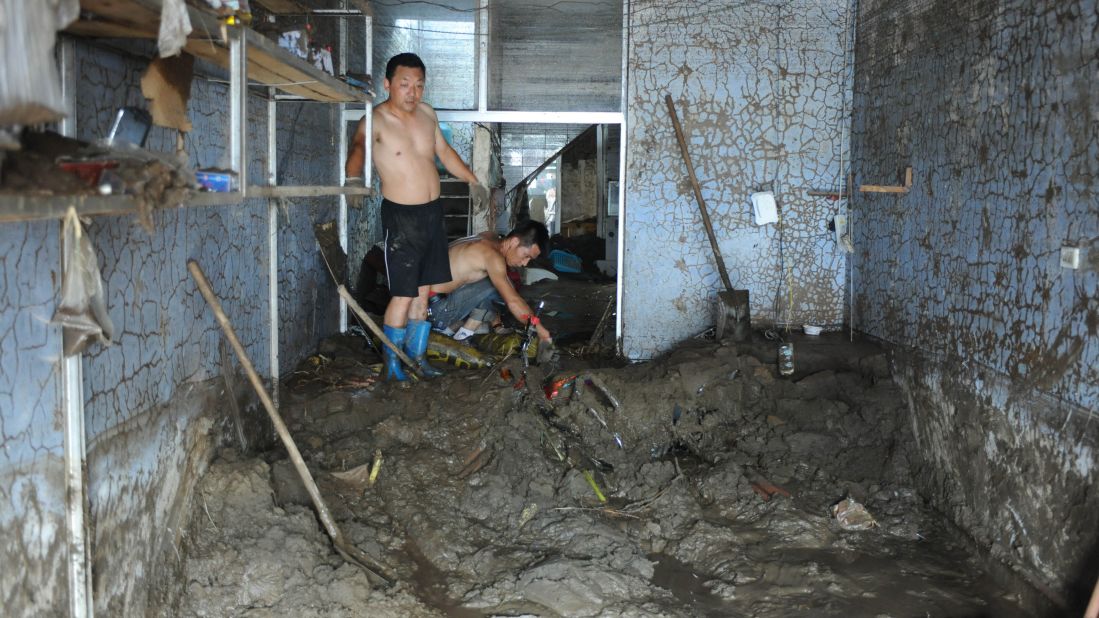 Men attempt to clean a building in Fushun City, China, on Tuesday, August 20. At least 107 people are dead in China after heavy rains inundated roads and farmland, the Chinese government says.