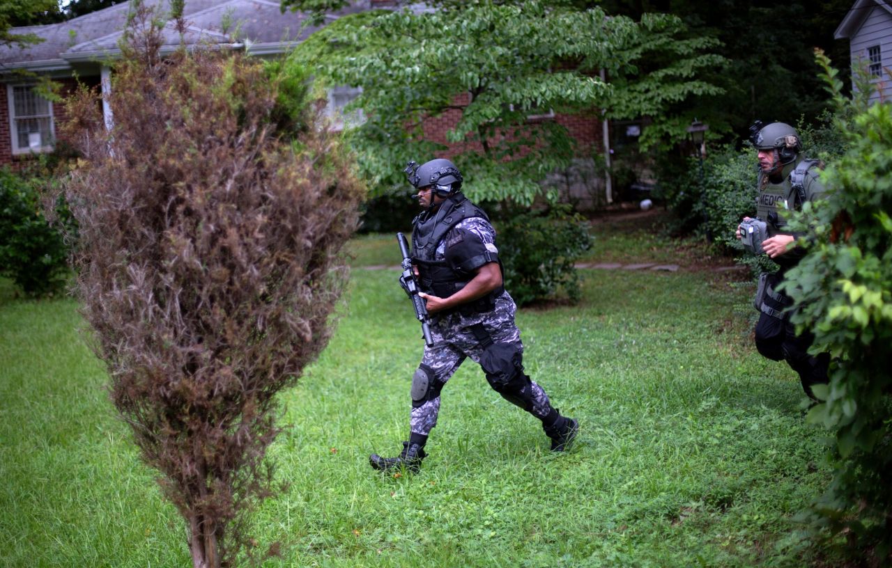 Dekalb County Police SWAT officers run though the front yard of a home toward the elementary school on Tuesday.