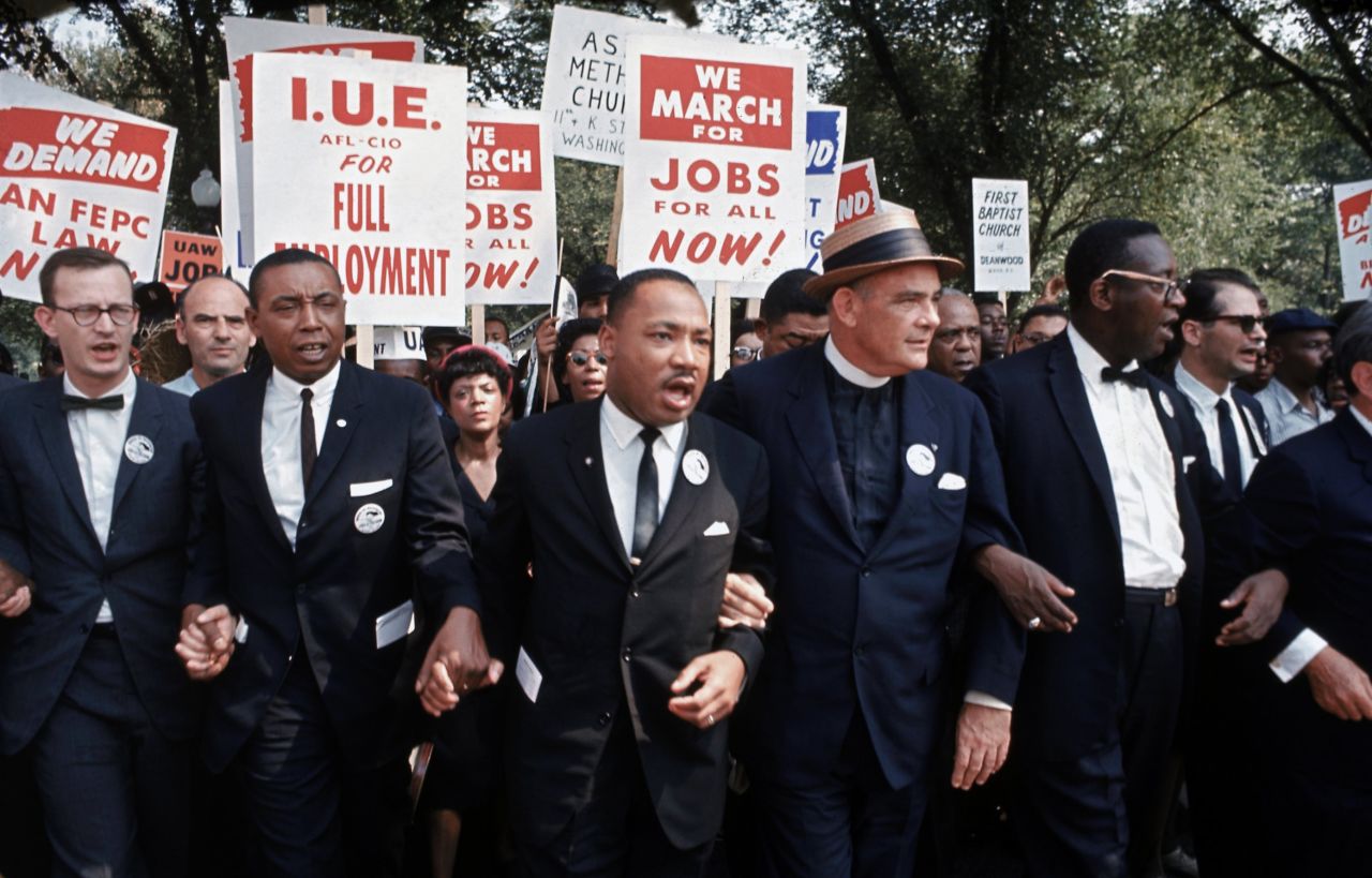 Leaders of the rally, including King in the center, interlock hands and arms as they march. The march was organized jointly by James Farmer, of the Congress of Racial Equality; Dr. King, of the Southern Christian Leadership Conference; John Lewis, of the Student Nonviolent Coordinating Committee; A. Philip Randolph, of the Brotherhood of Sleeping Car Porters; Roy Wilkins, of the National Association for the Advancement of Colored People; and Whitney Young, Jr., of the National Urban League.