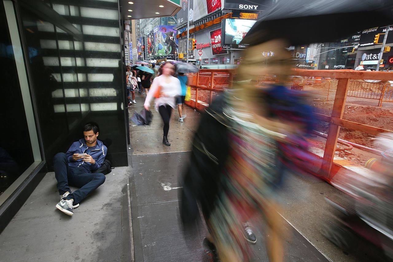 A man checks his cell phone from the shelter of a building as pedestrians walk in the rain in Times Square in New York on August 22. 
