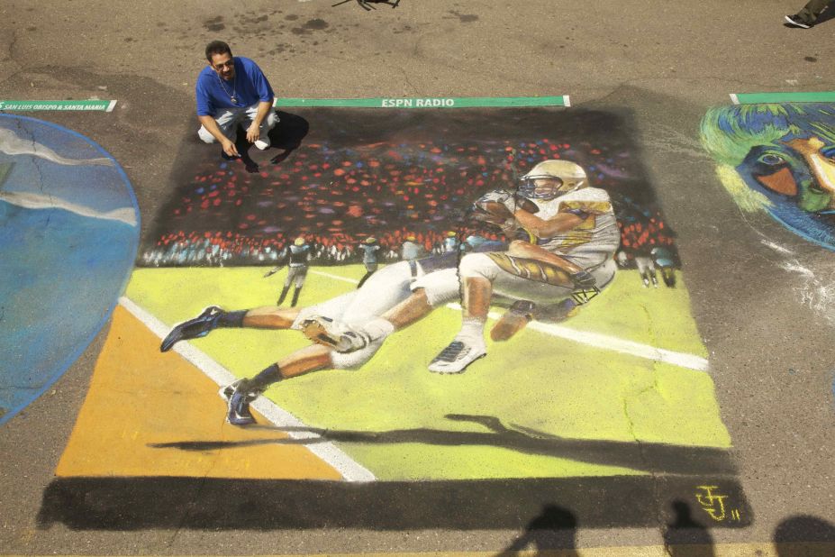 Artist Julio Jimenez crouches next to his image of a touchdown-saving tackle in San Luis Obispo, California.