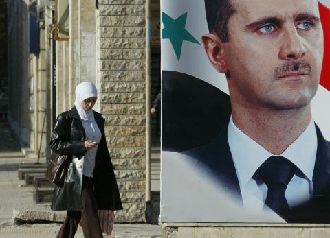 A Syrian woman walks past a large portrait of President al-Assad in downtown Damascus on December 13, 2005.