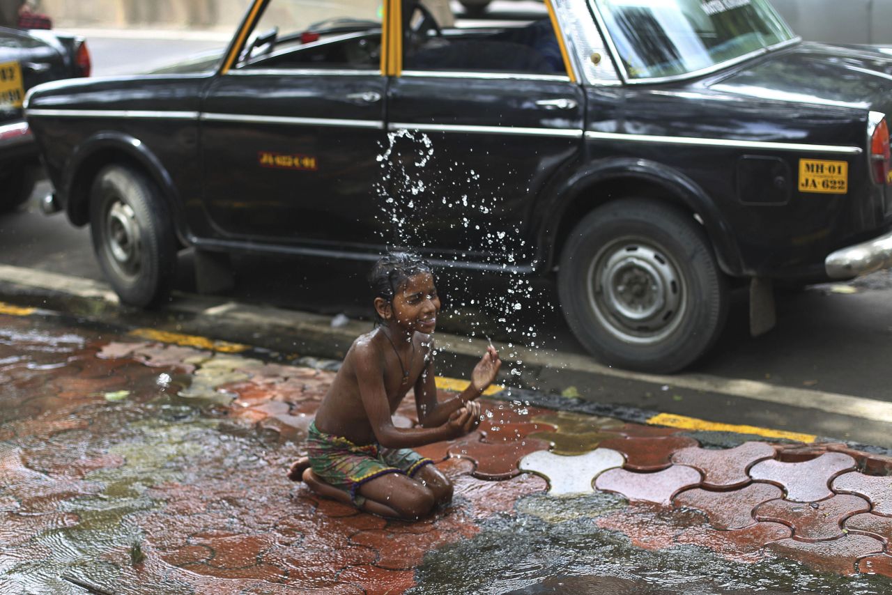 A boy plays with water flowing from a broken tap on a pavement in Mumbai, India, on August 28.