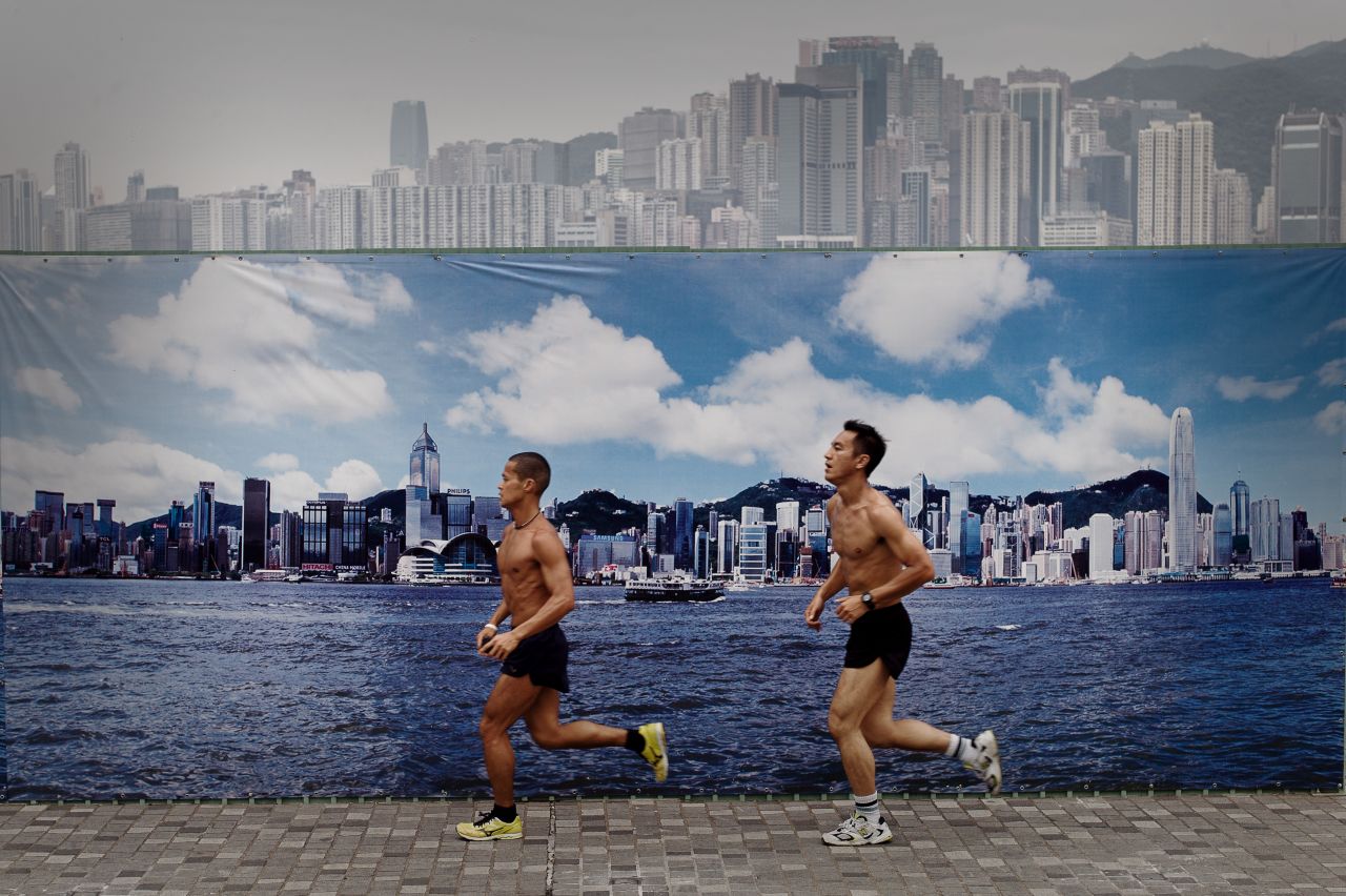Two men jog past a billboard featuring photos of the city skyline with a clear sky on a cloudy day in Hong Kong on August 30. The billboard erected along the Avenue of Stars attracts tourists who find it more appealing to pose for photographs in front of it than the city's skyline on a cloudy or polluted day. 
