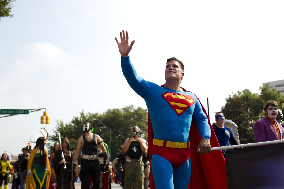 A man dressed as Super-Man walks in the parade with other characters from DC Comics.