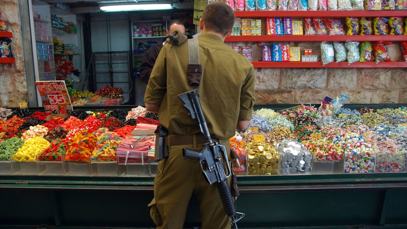 In among the holy sites, daily life roars on: Souks crowd the narrow, stone-flagged alleyways; children go to school; libraries jostle with restaurants. Here, a soldier buys candy at the Mahane Yehuda Market. 