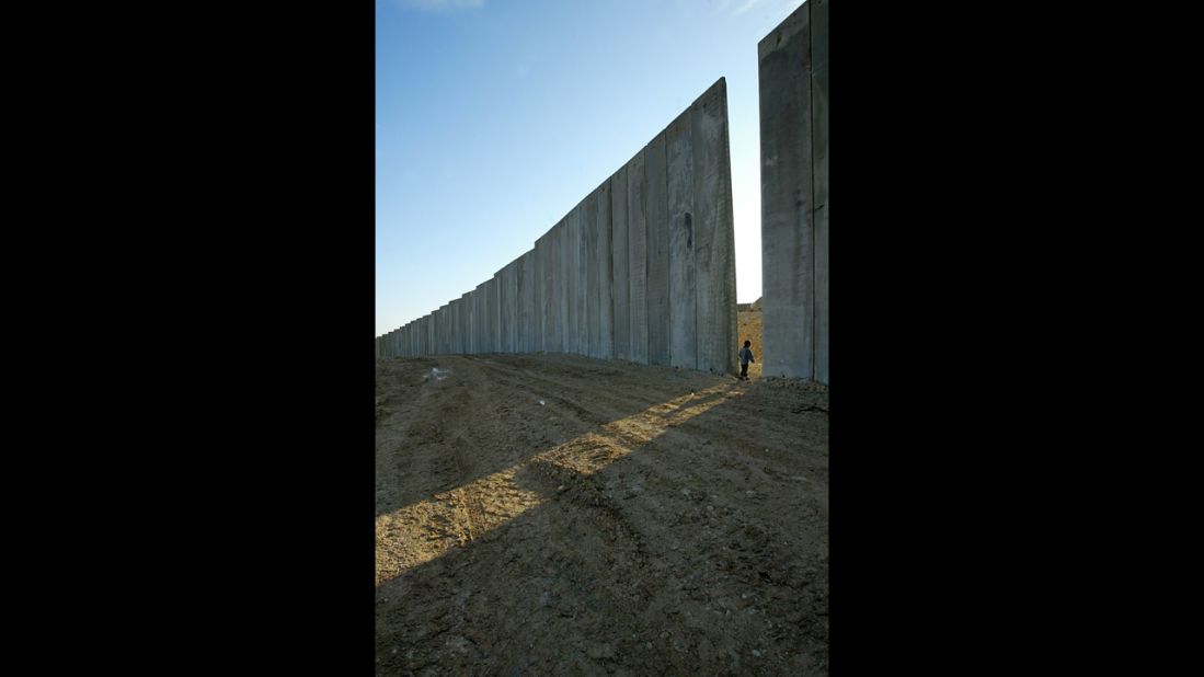 A child walks through a gap in the concrete blocks of a security wall in the W
