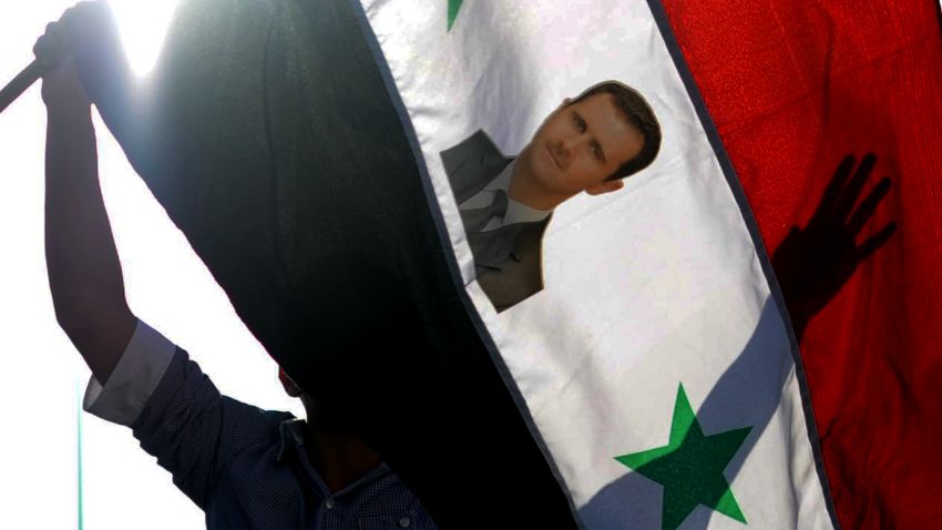   A protester waves a Syrian flag with the photograph of Syrian President Bashar al-Assad during a rally against a possible attack on Syria in response to alleged use of chemical weapons by the Assad government on September 1, 2013, in Hatay. 