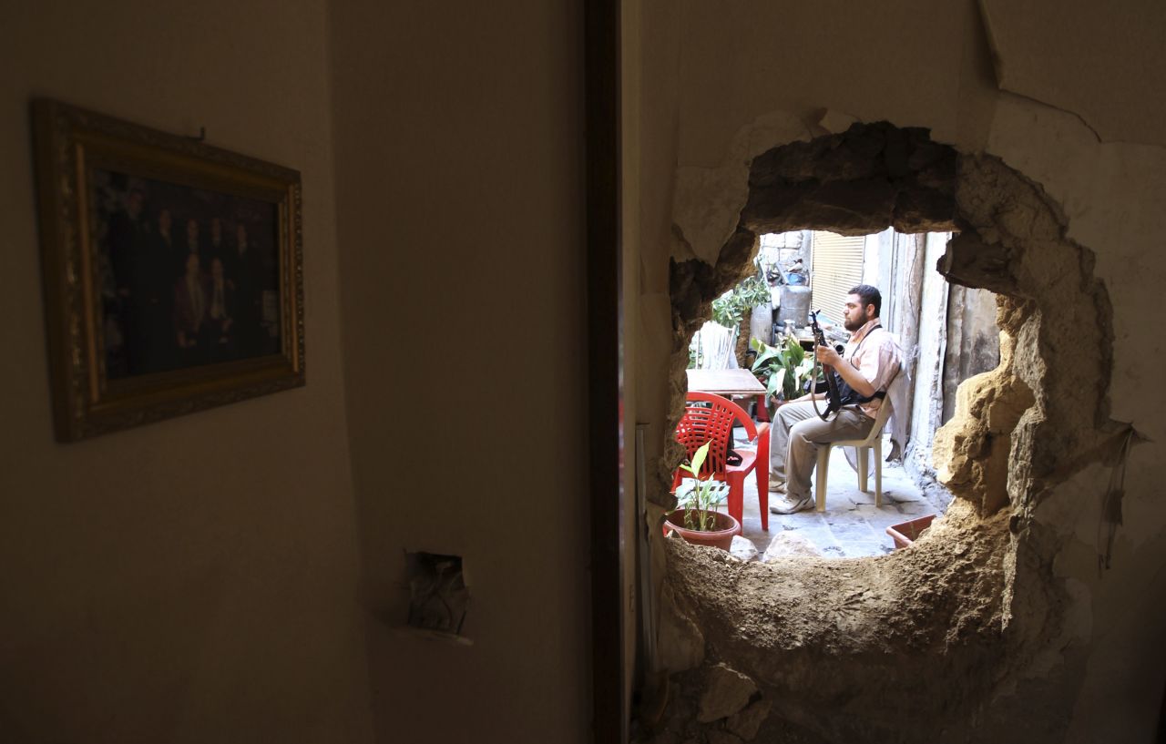 Un combatiente sirio se ve a través de un agujero en una pared de un edificio en Alepo, mientras hace guardia.