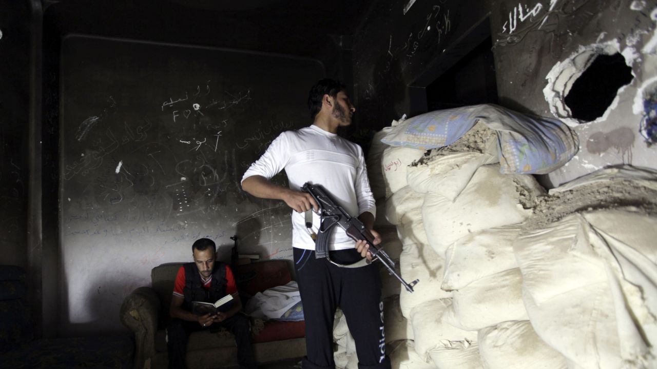 Un combatiente opositor mira a través de un agujero por detrás de sacos de arena, mientras que un compañero lee el Corán en Deir Ezzor, Siria, el martes 3 de septiembre.