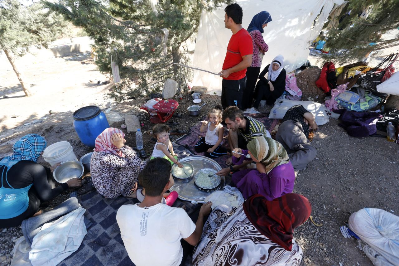 Syrian refugees who failed to find shelters at a refugee camp eat and rest by the side of a road a few feet away in September 2013.