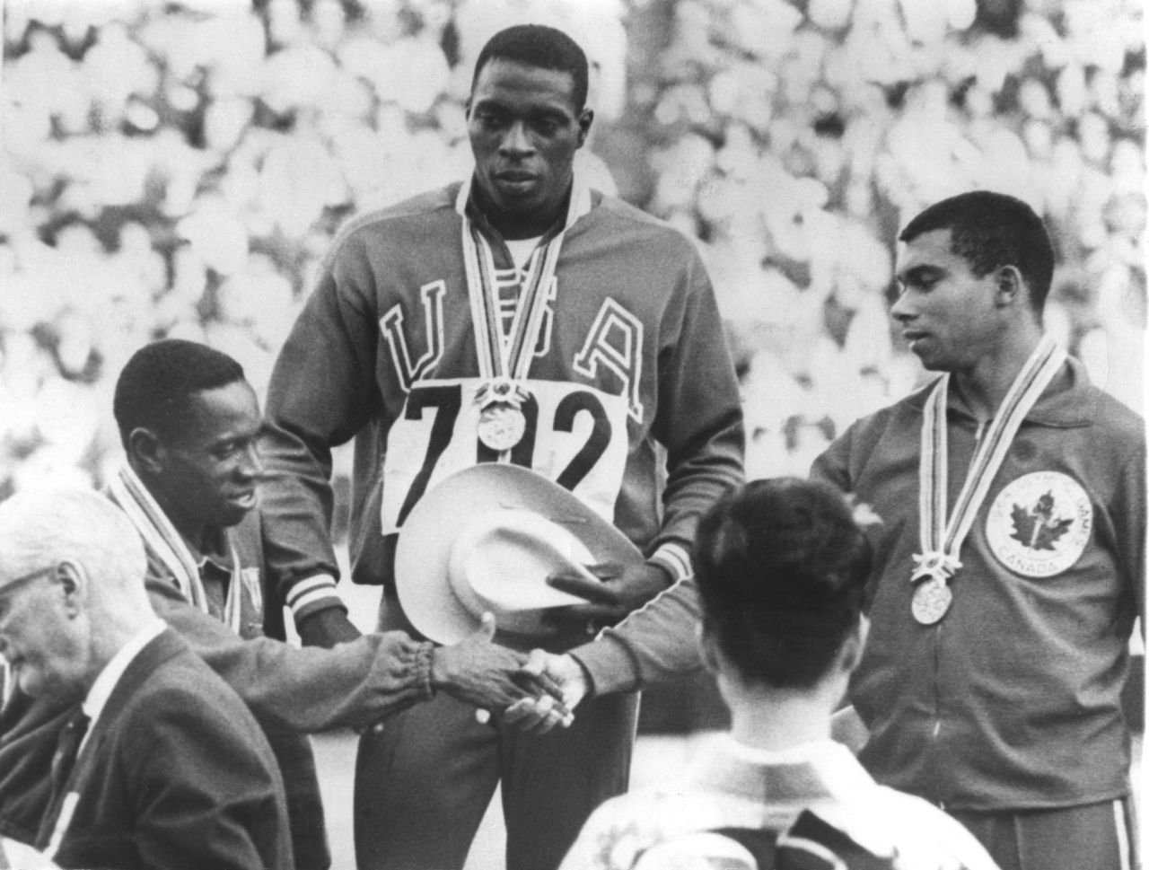 October 15, 1964: Robert Hayes of the U.S. (center) stands on the podium after receiving his gold medal for winning the men's 100 meter final. Silver medal winner Enrique Figuerola of Cuba (left) congratulates Harry Jerome of Canada, who came third. Hayes' time of 10.0 seconds was a new Olympic record. 