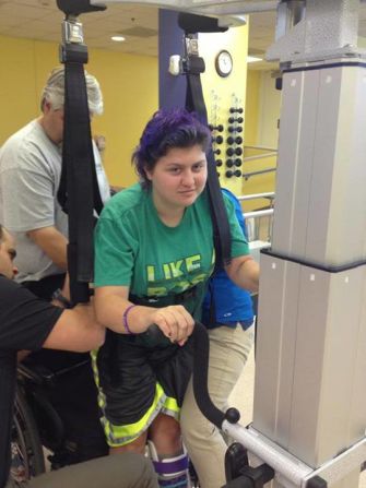 This contraption is helping Emily relearn how to walk. Here, her stepfather and physical therapists help strap her in on August 6.