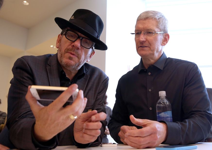 Rocker Elvis Costello, who played a few songs at the event, examines a new iPhone as Tim Cook looks on.