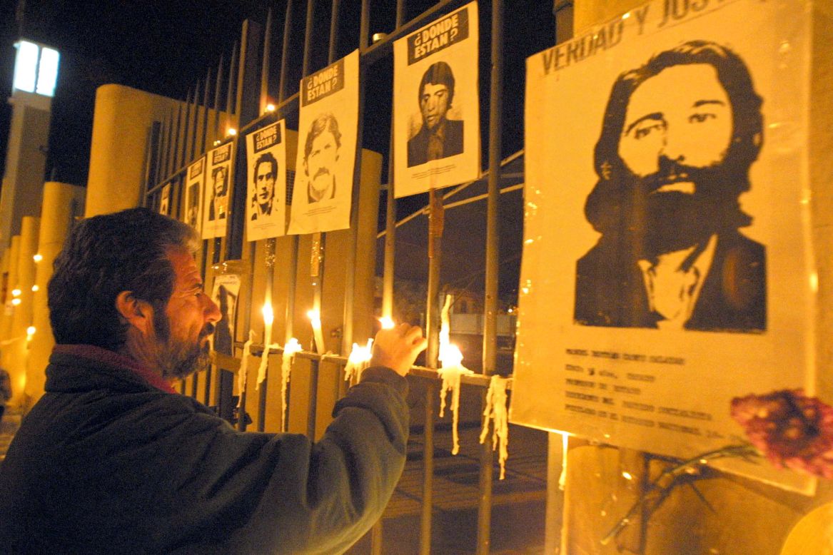 A man lights a candle at the gates of the National Stadium on September 11, 2002 in Santiago bearing pictures of those who disappeared under the 1973-1990 dictatorship of Pinochet. 