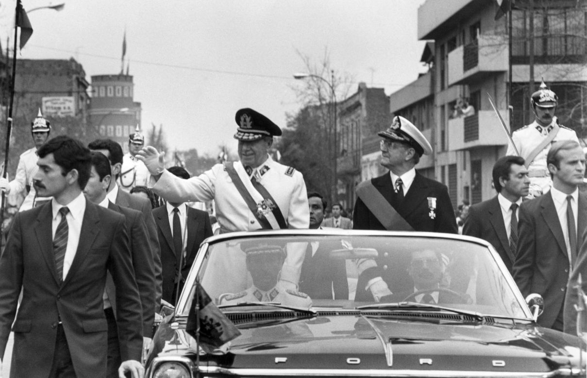 General Augusto Pinochet, standing in a white jacket, a career army officer, led the military coup and established himself as the head of the ensuing government. He waves from the motorcade on September 11, 1973 in Santiago, accompanied by the Chilean defense minister, Vice-admiral Patricio Carvajal. A year later, in 1974, Pinochet signed a decree naming himself Chilean president.
