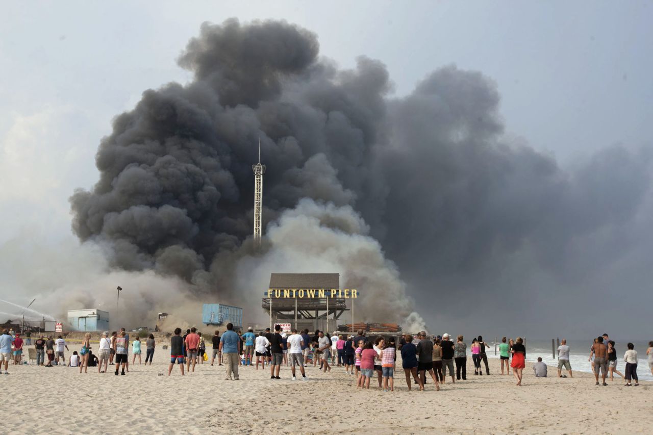 Onlookers line the beach as smoke rises from the boardwalk. 