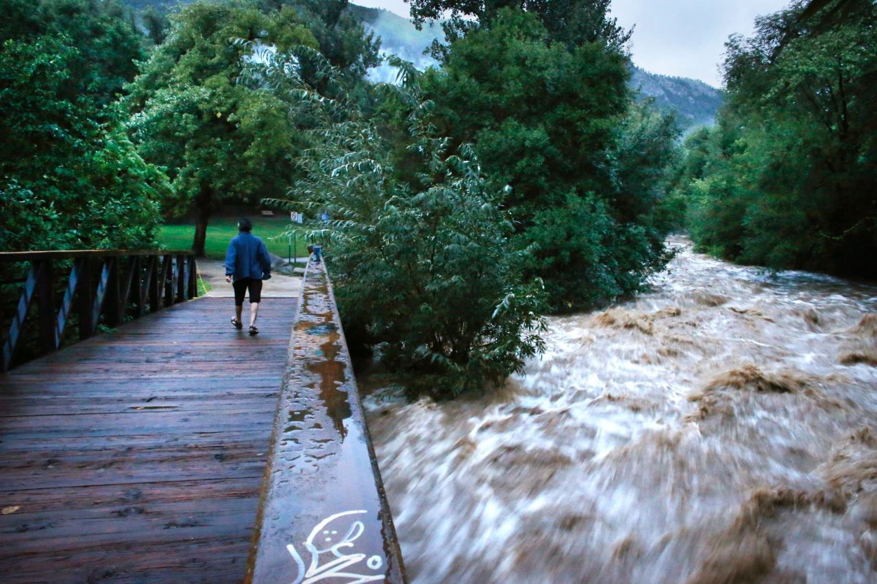 During a break in the rain, a woman walks over a footbridge past the raging Boulder Creek in Boulder on September 13. Boulder County is one of the hardest-hit areas.