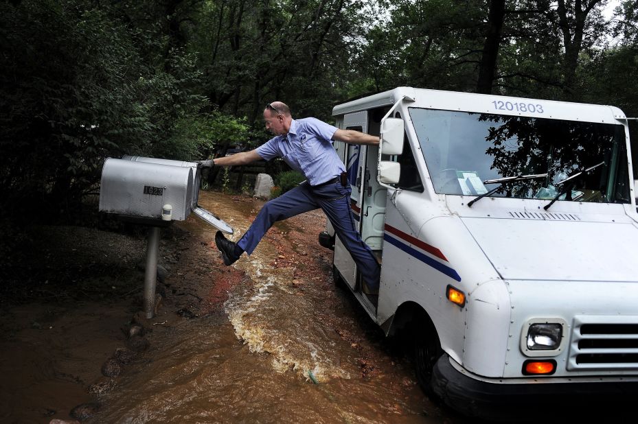 Dave Jackson closes a mailbox with his foot after delivering the mail to a home surrounded by water from the flooded Cheyenne Creek in Colorado Springs, Colorado, on Friday, September 13.