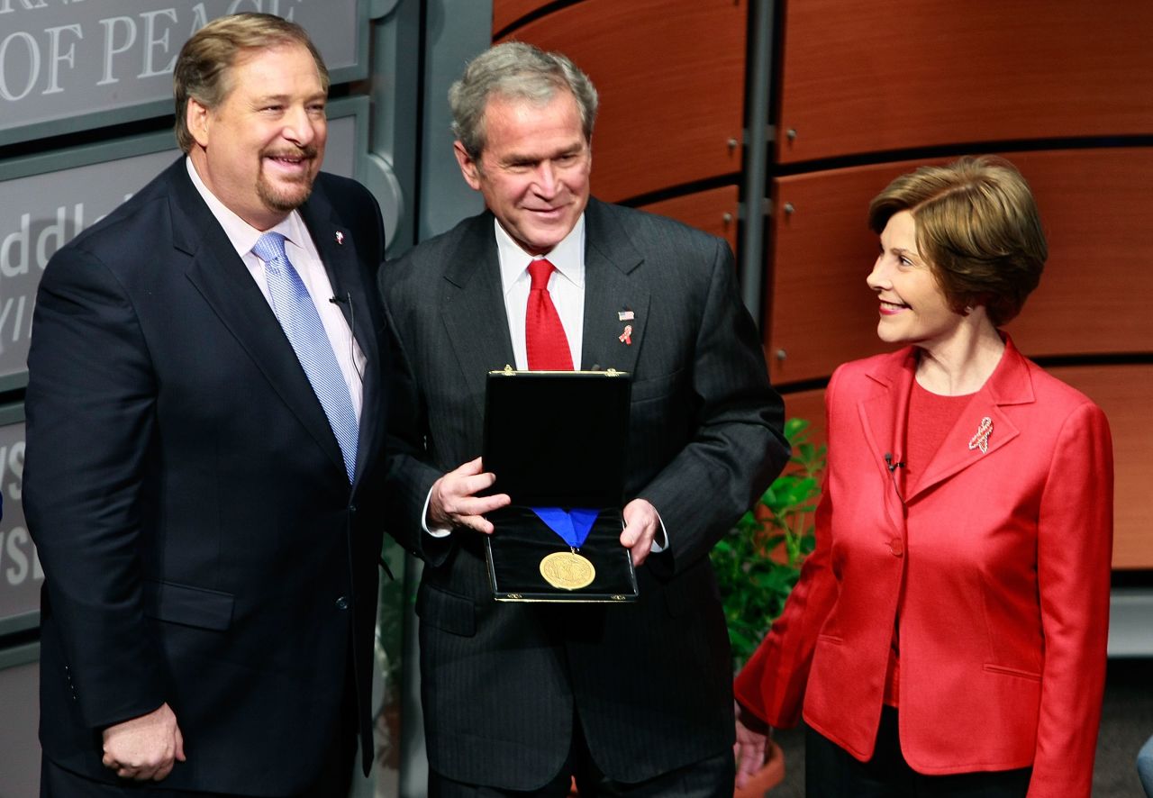 Warren presents President George W. Bush with the International Medal of P.E.A.C.E, as Laura Bush looks on, during the Saddleback Civil Forum on Global Health at the Newseum in Washington on December 1, 2008. The award was in recognition of an initiative to provide funding for treatment for 2 million people with HIV/AIDS by the end of 2008. The acronym P.E.A.C.E. stands for: Promote reconciliation. Equip servant leaders, Assist the poor, Care for the sick, Educate the next generation.