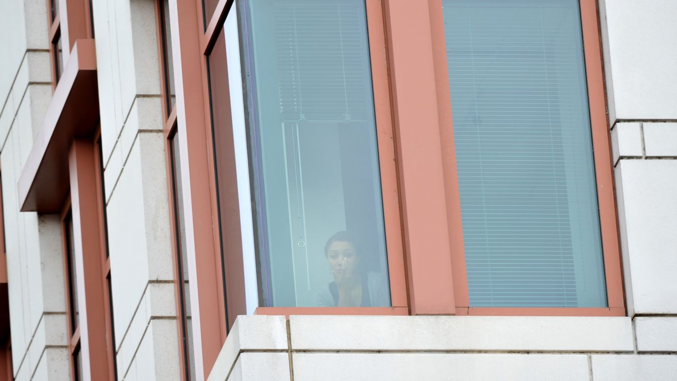A woman watches from an office building as police respond to the shooting.