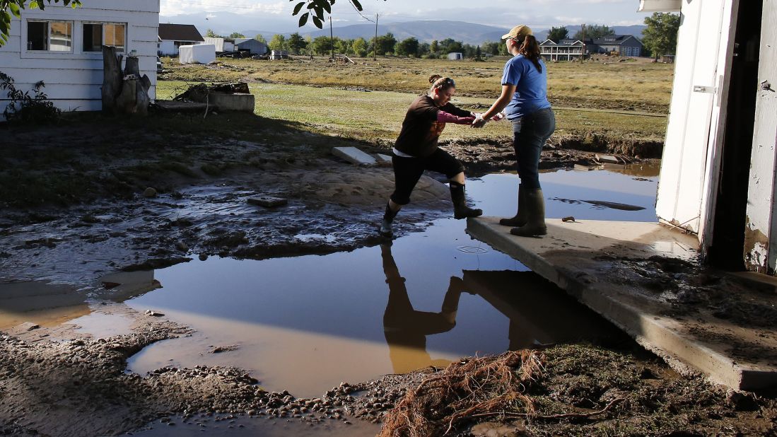 A woman steps over a puddle onto the foundation of a shed that was moved by floodwaters in Hygiene, Colorado, on Monday, September 16.