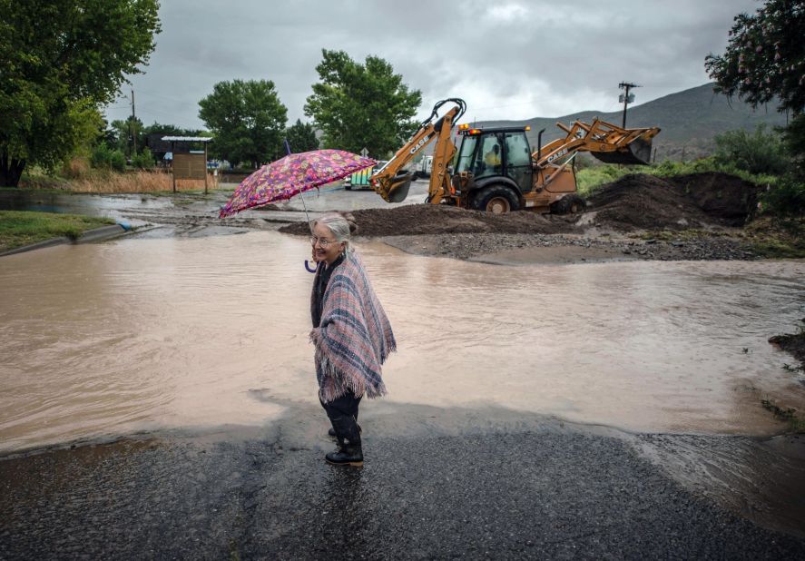 Candie Browne dips her boot in water to clean off the mud as a backhoe in the background builds a levy to redirect rainwater from flooding a park near downtown Truth or Consequences, New Mexico, on Friday, September 13.
