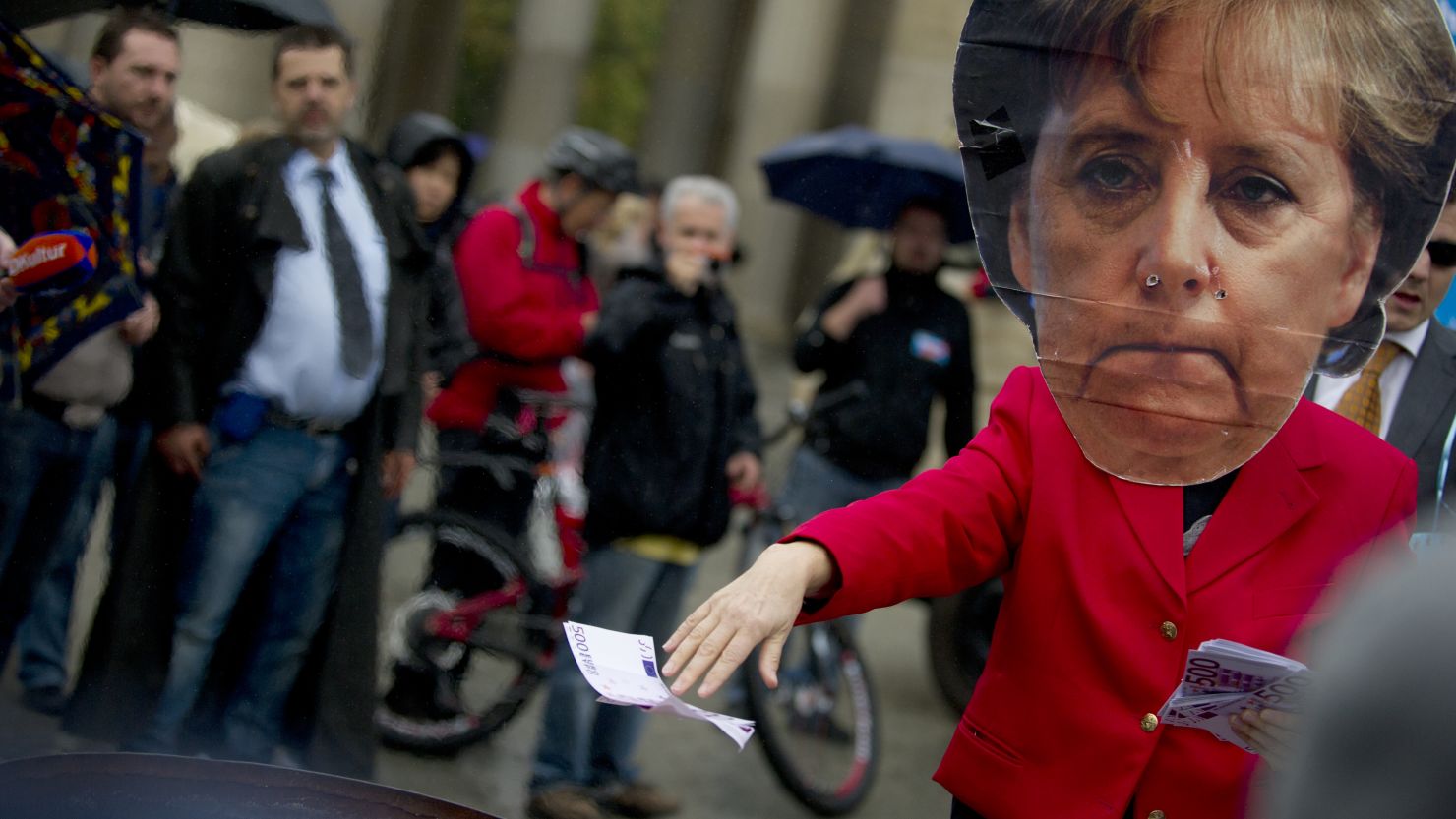 A person wearing an Angela Merkel mask throws fake euros at an anti-euro Alternative for Germany (AfD) rally.