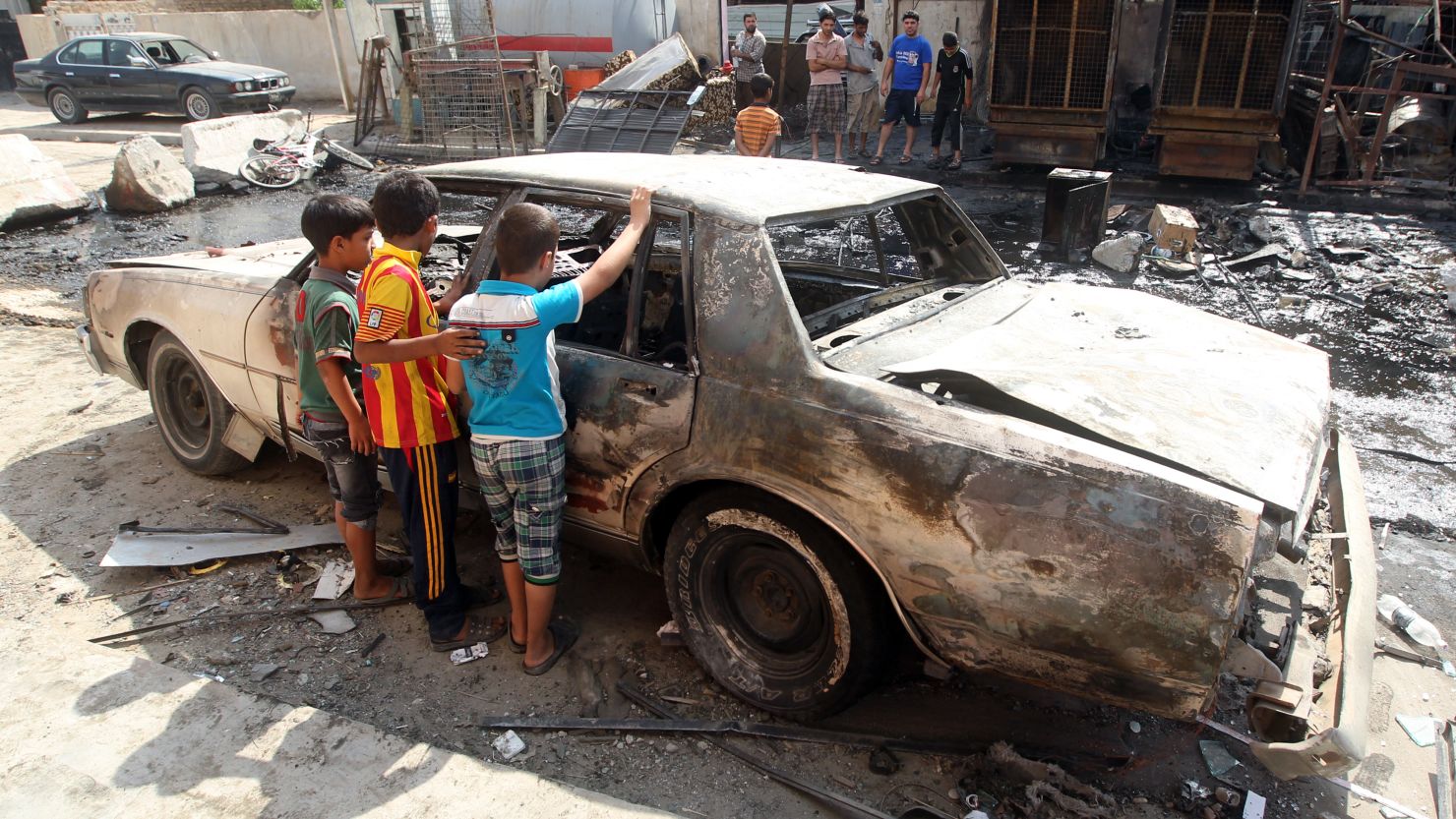 Children inspect a burned-out car after a car bomb exploded the previous day in Mashtal on September 16, 2013.