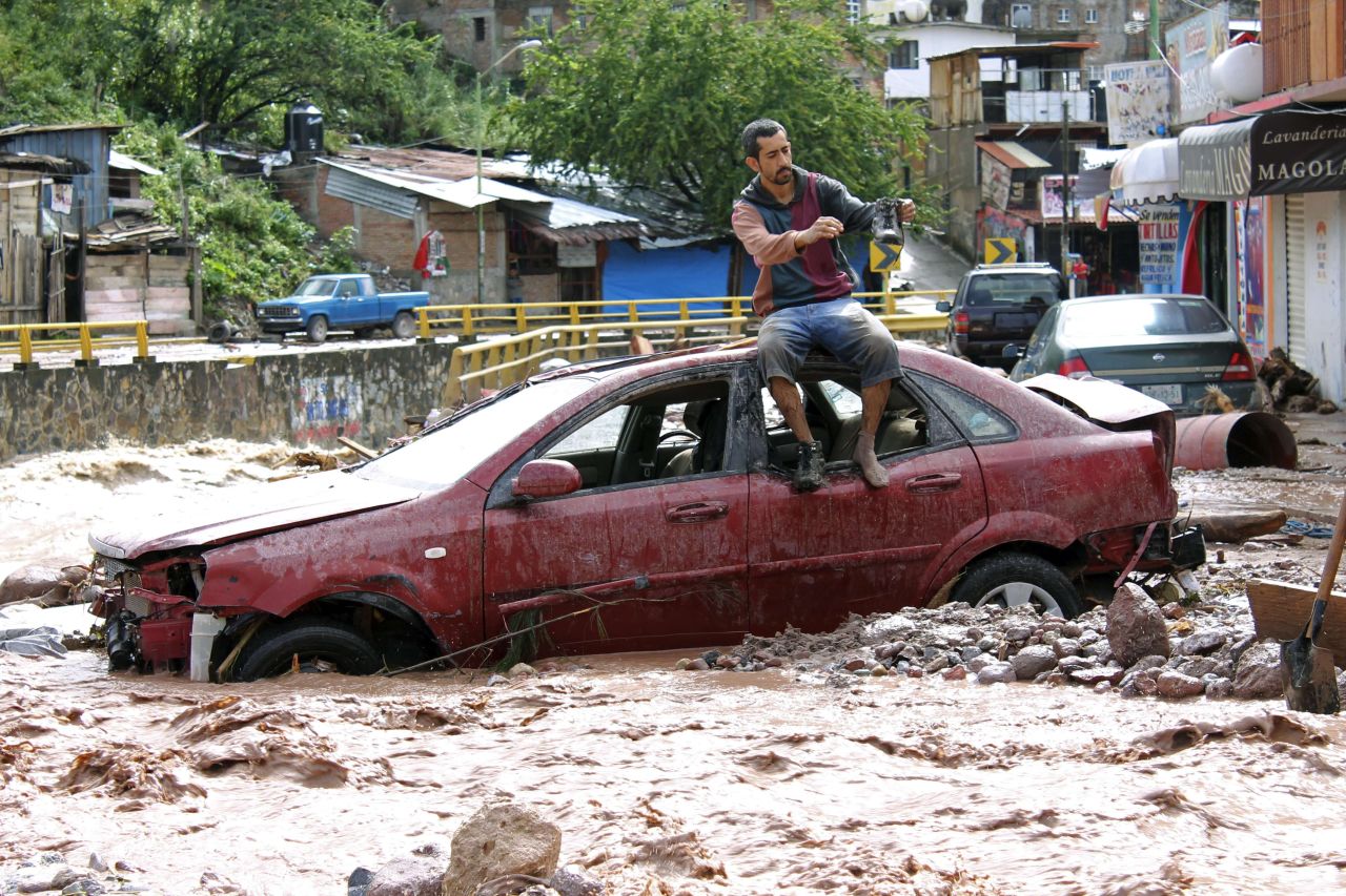 Un hombre se sienta sobre una carro mientras intenta cruzar una calle inundada en la Chilpancingo, estado Guerrero.<br />