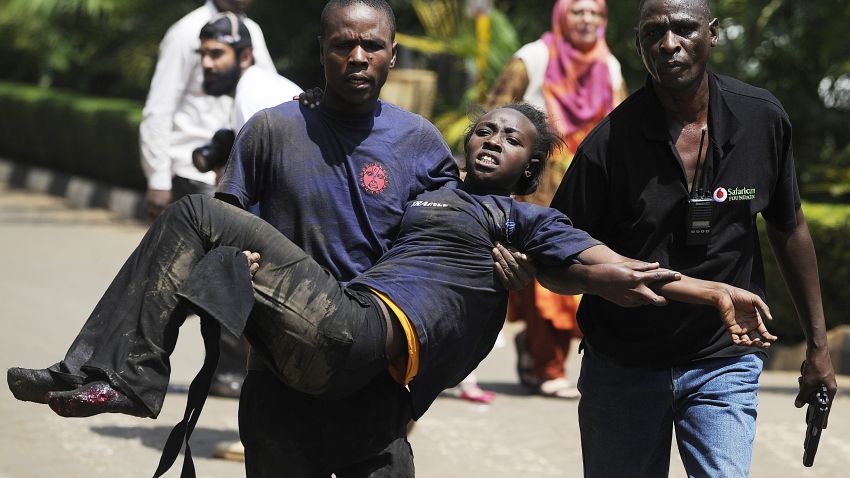 A Kenyan woman is helped to safety after masked gunmen stormed an upmarket mall and sprayed gunfire on shoppers and staff, killing at least six on September 21, 2013 in Nairobi. The Gunmen have taken at least seven hostages, police and security guards told an AFP reporter at the scene. AFP PHOTO/SIMON MAINA        (Photo credit should read SIMON MAINA/AFP/Getty Images)
