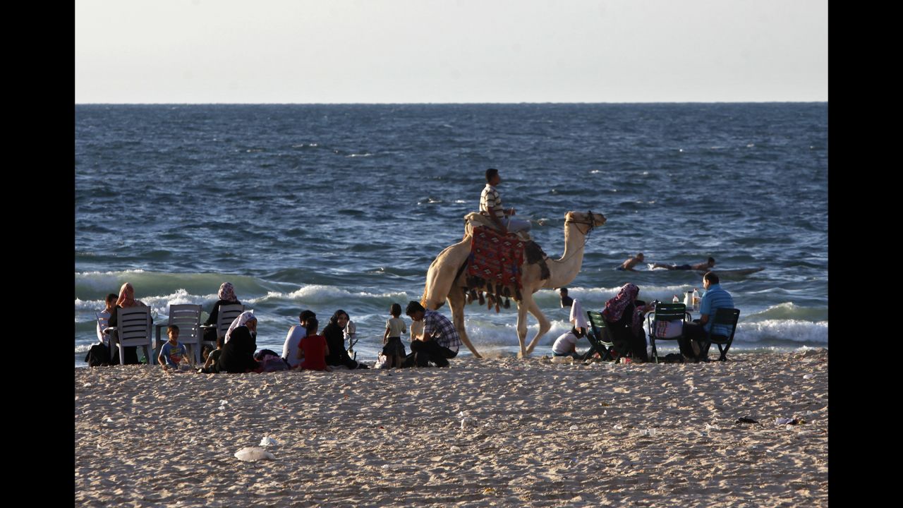 A Palestinian rides a camel along the beach of the Mediterranean Sea as families enjoy the sunset on Friday, September 20, in Gaza City.