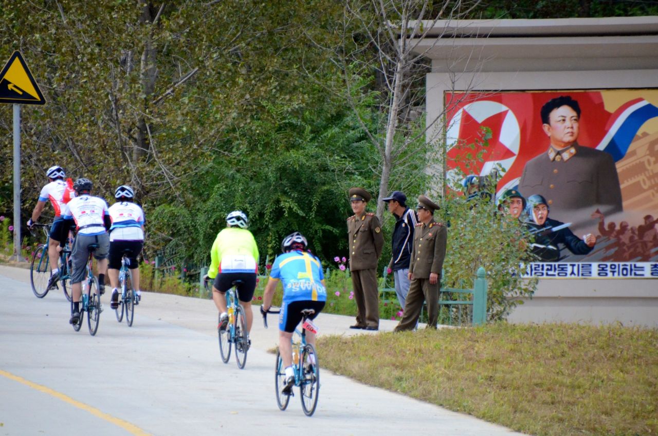 Riders passing a propaganda monument of Dear Leader Kim Jong-il.