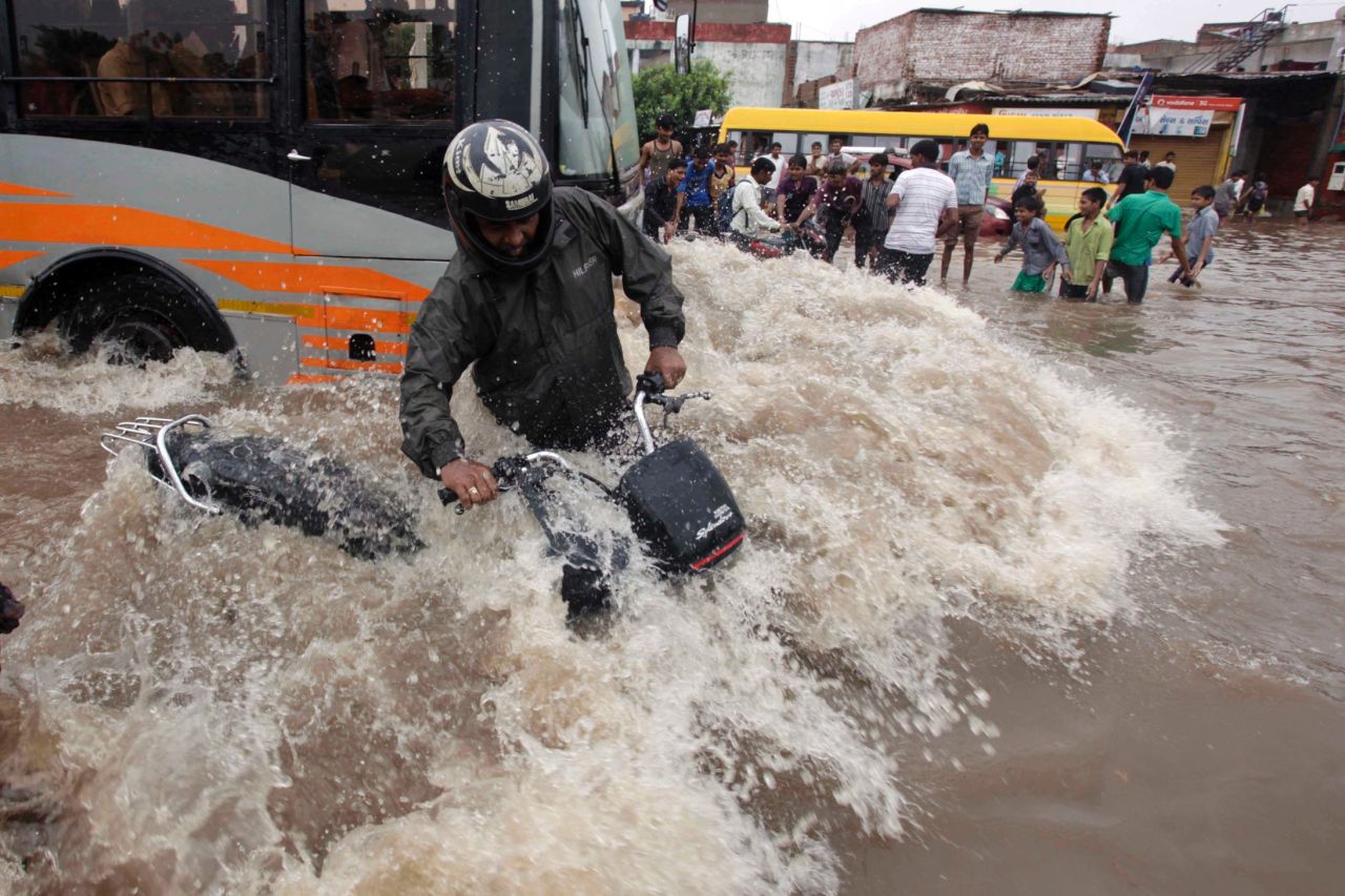 An Indian motorist tries to balance himself as a bus drives past on a flooded road in Ahmadabad, India, on September 25.