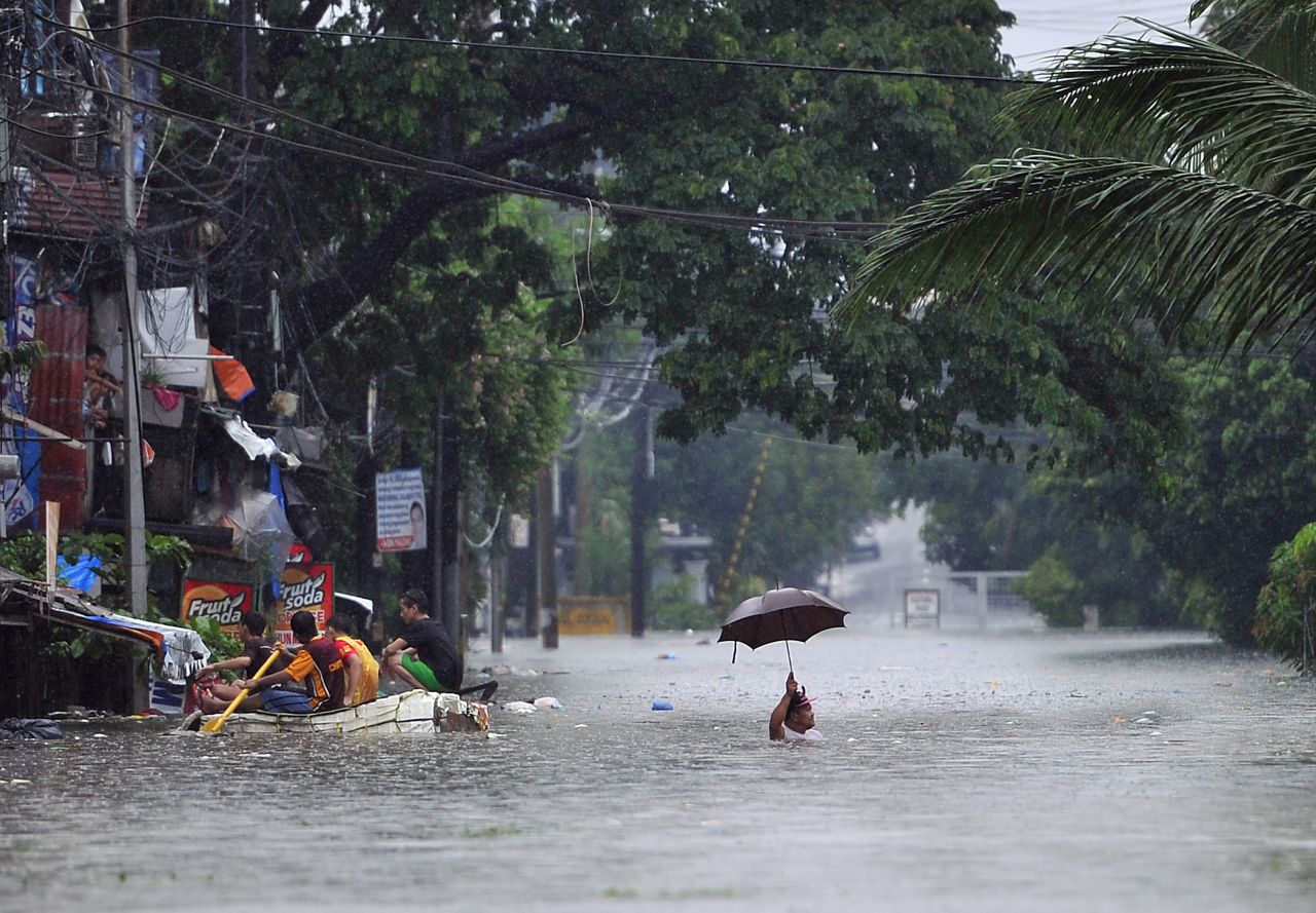 A resident wades through chest-deep flood waters along a street in Manila while his neighbors paddle an improvised raft on September 23.