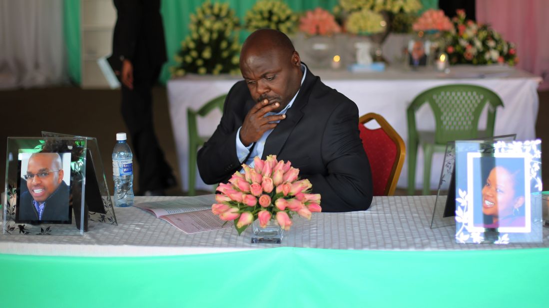 A man sits at a table with photos of Mbugua Mwangi and Mwangi's fiancee, Rosemary Wahito, during their funeral service in Nairobi on Friday, September 27. Mwangi was the nephew of Kenyan President Uhuru Kenyatta's.