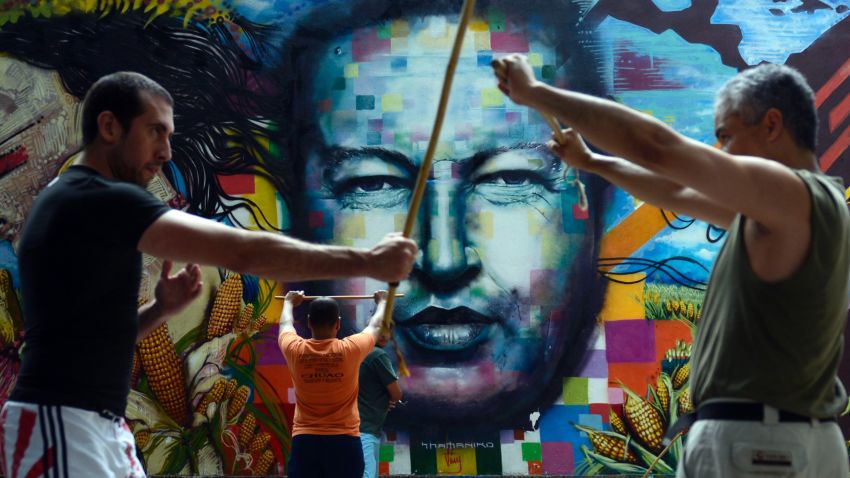 People train stick fight in front of a mural depicting late Venezuelan former President Hugo Chavez in Caracas on August, 18, 2013.