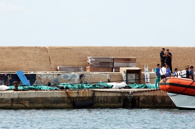 Italian police and rescue workers stand next to the covered bodies of migrants at the port of Lampedusa on October 3.