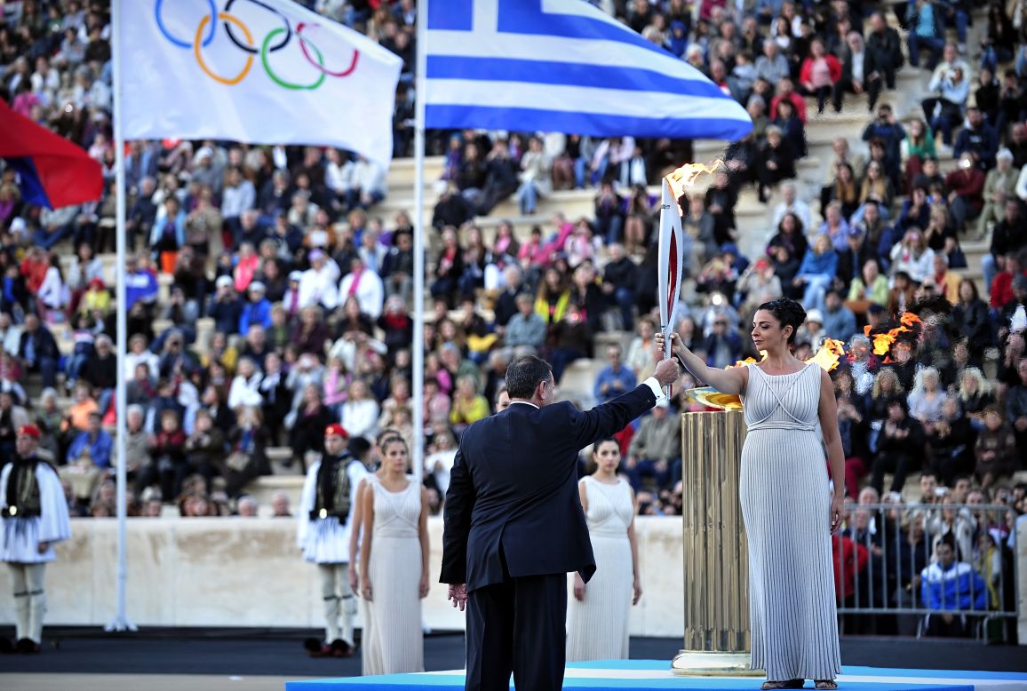 Actress Ino Menegaki, playing a high priestess, hands the Olympic flame to the president of the Hellenic Olympic Committee, Spyros Kapralos, at the Panathenaic stadium in Athens.