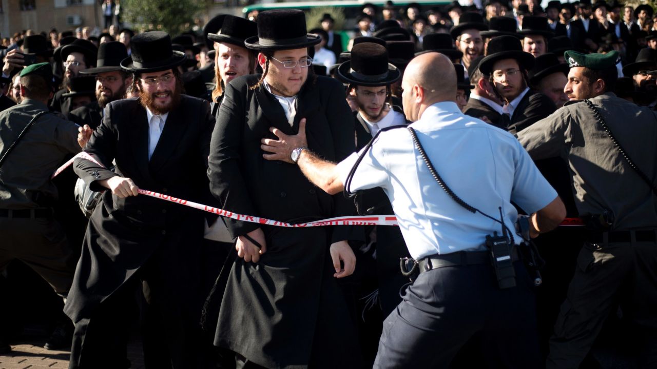 Police try to hold back Orthodox men and children from reaching the vehicle carrying the rabbi's body.