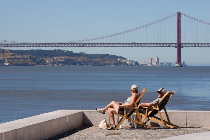 Tourists sit in the sun at Cais do Sodre overlooking the River Tagus and the "25th of April Bridge" bridge in Lisbon, Portugal. Once known for its seedy bars and brothels, today it boasts hot clubs and great restaurants. 