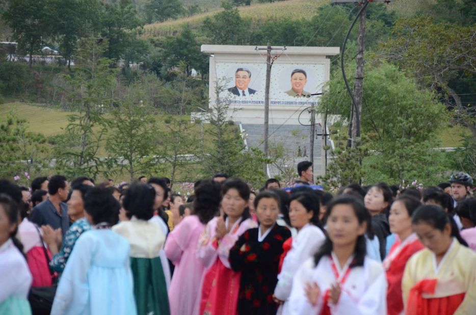 Spectators waiting for the bikers to reach the finish line. In the background the "Great" and "Dear Leaders" Kim Il Sung and his son, Kim Jong-Il.