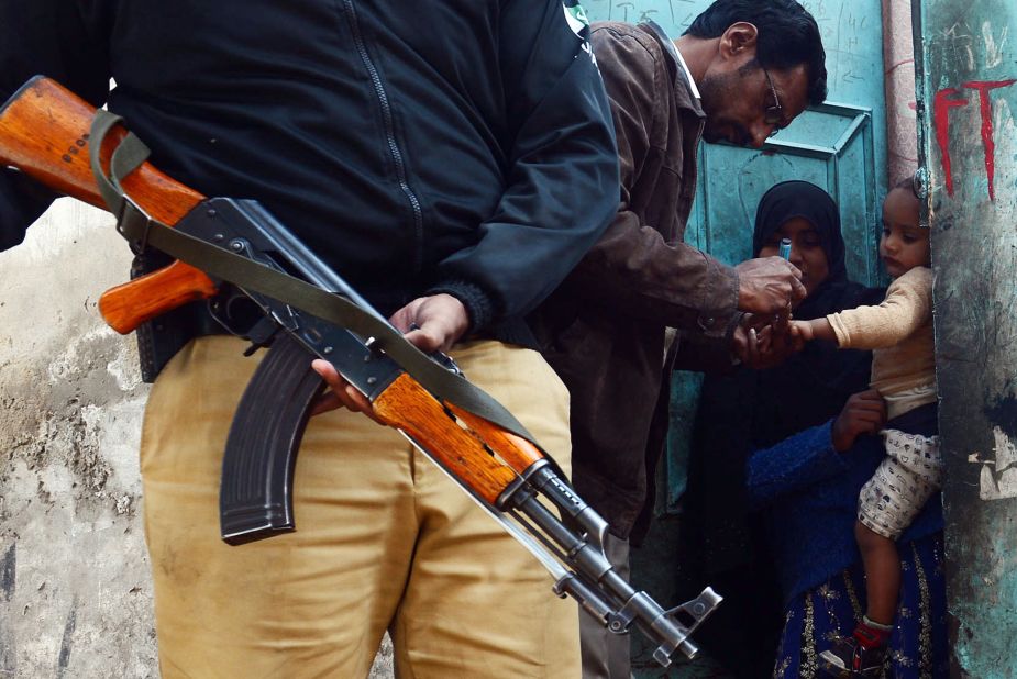 Efforts to stamp out the crippling disease have been hampered by resistance from the Taliban, who have banned vaccination teams from some areas. A Pakistani policeman stands guard as a polio vaccination worker marks a child after immunization with anti-polio drops an infant in Lahore on December 21, 2012.
