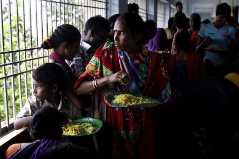 Evacuated villagers watch the strong winds and rain as they eat a meal in a temporary cyclone shelter in the town of Chatrapur, India, on October 12.