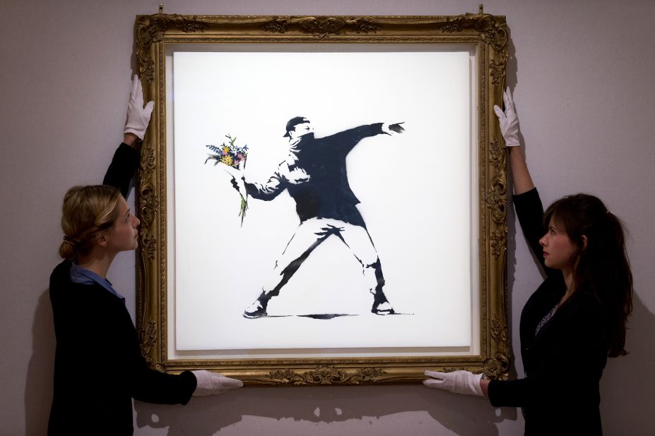 Gallery assistants adjust Banksy's "Love Is in the Air" ahead of an auction in London in June 2013. The piece was sold for $248,776.