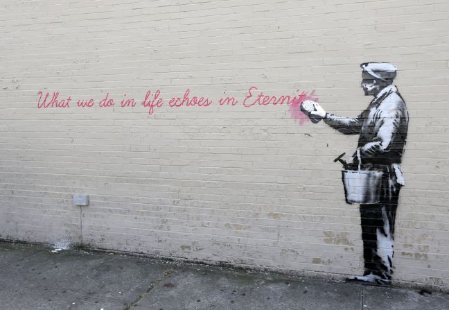 A Banksy mural on a wall in Queens shows a man washing away a quote from the movie "Gladiator." It reads: "What we do in life echoes in eternity."