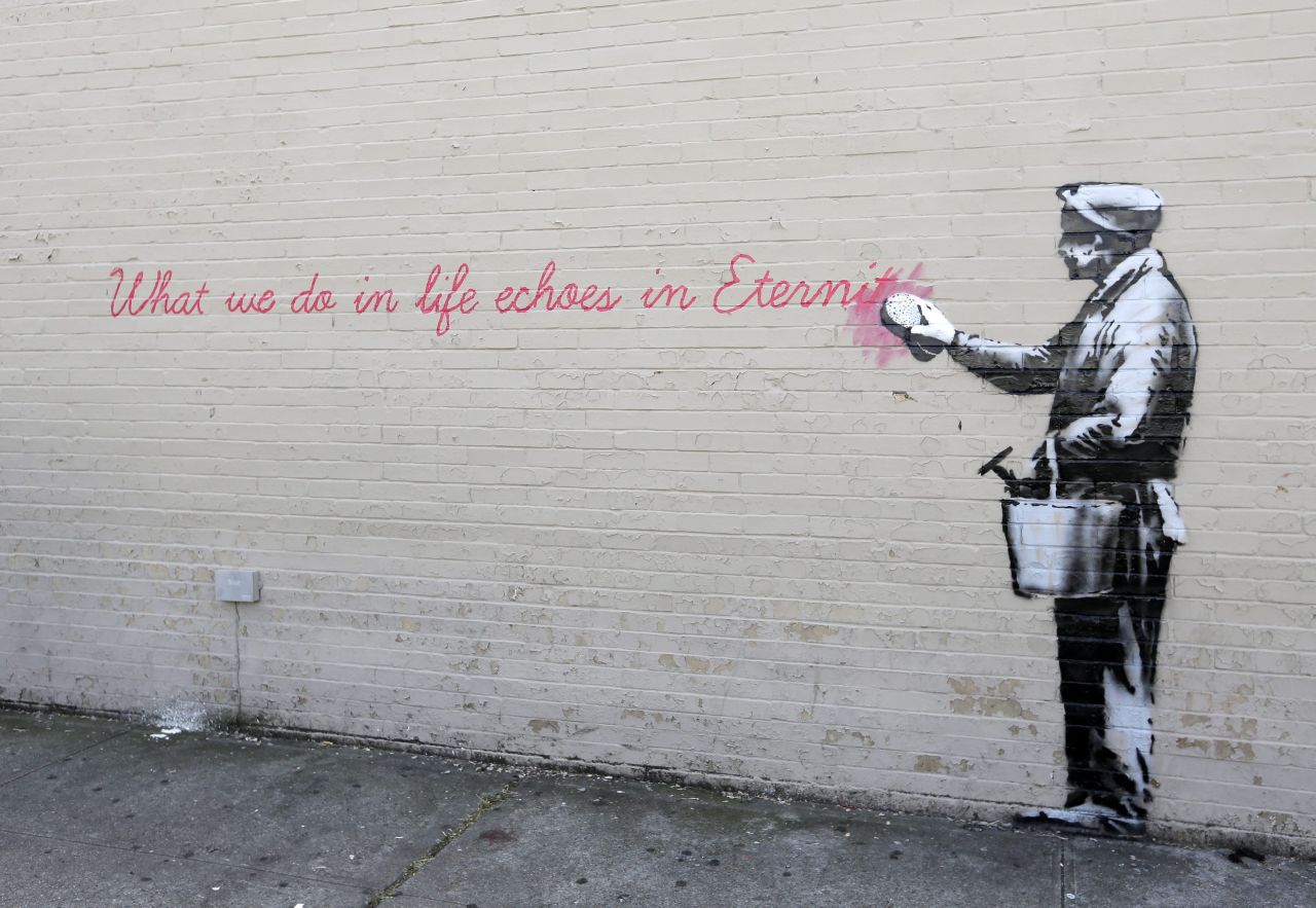 A Banksy mural is seen on a wall in Queens. The quote is from the movie "Gladiator." It says, "What we do in life echoes in eternity."