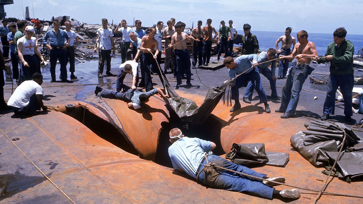 Crew members look through a hole in the deck of the USS Forrestal in search of survivors after the explosion in July 1967.