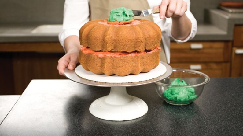 Place the second cupcake cut side down on top of the frosting to create the stem. Completely cover the stem with green frosting. <a href="http://eatocracy.cnn.com/2013/10/24/pumpkin-cake/">See the full recipe.</a>